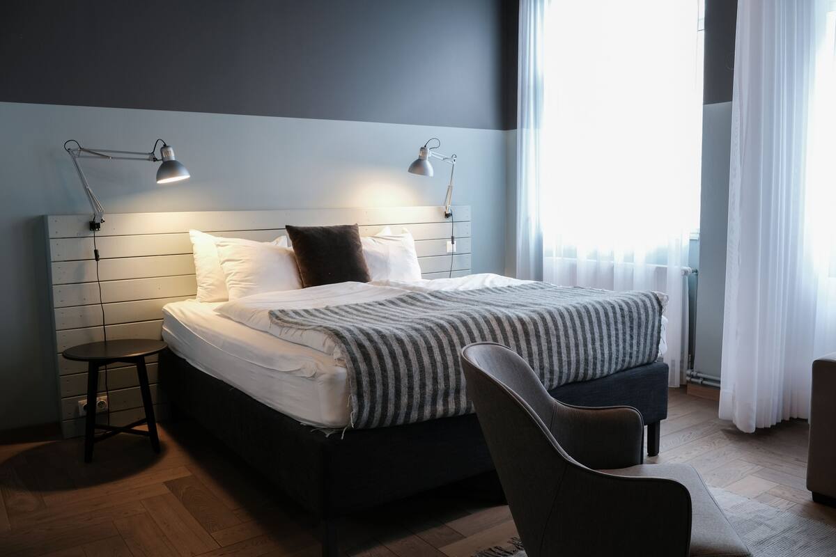 A modern bedroom with a bed, bedside lamps, a chair, and a window with curtains.