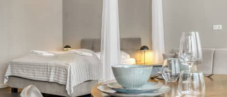 A hotel room with a bed, bedside table, and a dining table set with plates, glasses, and cutlery.