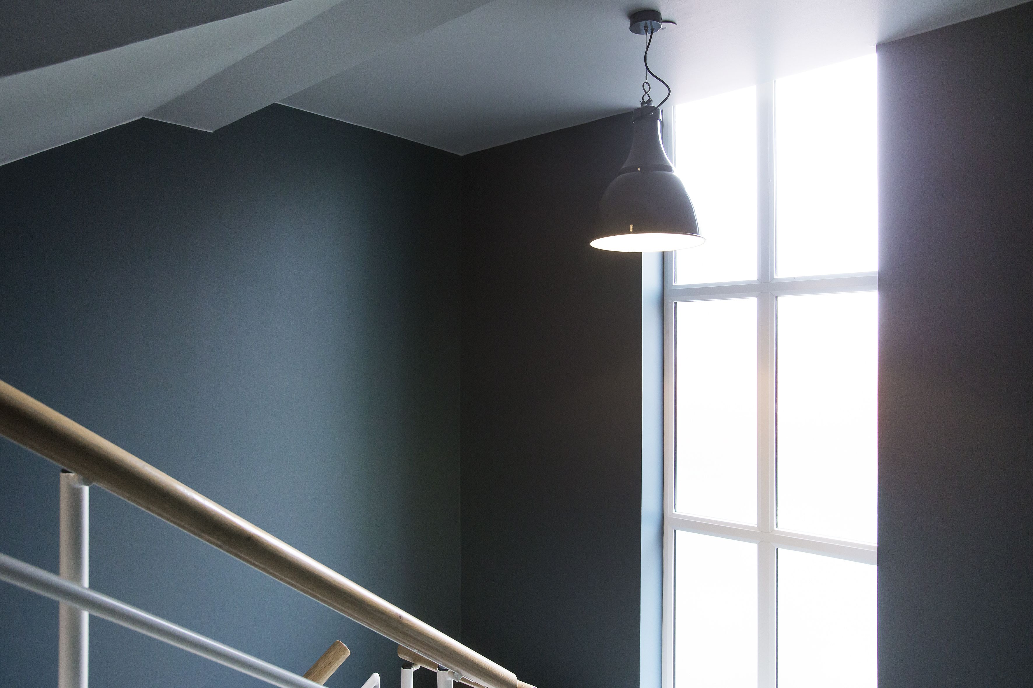 Eine Treppe mit Metallgeländer, einer dunklen Wand und einem Fenster mit Tageslicht.