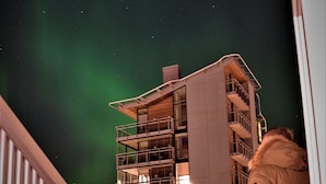A person standing on a balcony with a view of a building and the night sky.