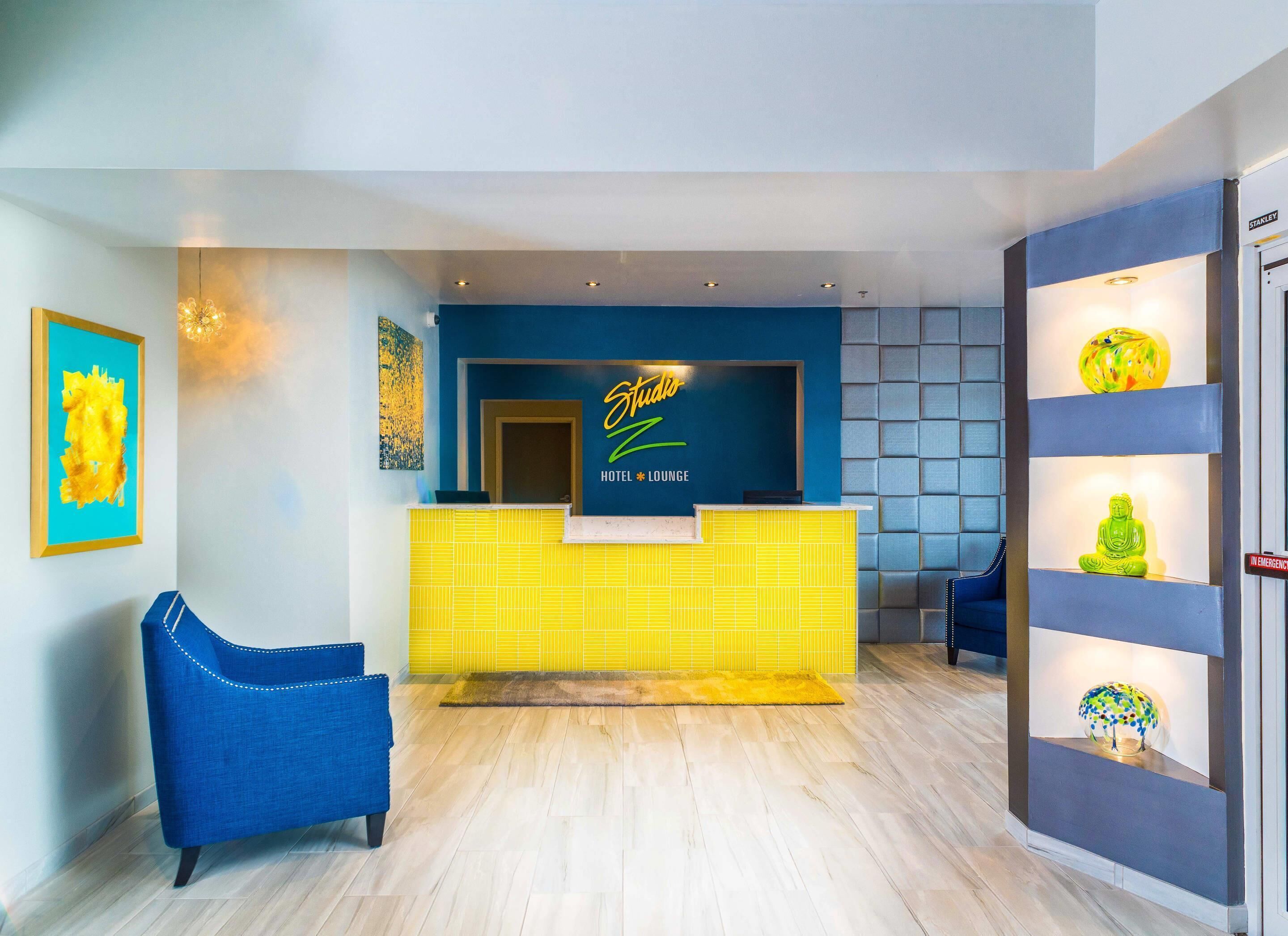 Un vestíbulo de hotel con mostrador de recepción, sillas azules, una estatua de Buda y una pared con un letrero Stanley.