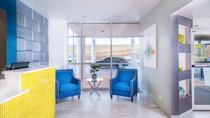 Un área de recepción de diseño moderno, con un mostrador de recepción, dos sillones azules, una pequeña mesa redonda con una planta y ventanas amplias que dan al estacionamiento.
