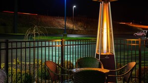 Escena nocturna con una estructura alta e iluminada, sillas de mimbre y vista a una carretera y paisaje distante.