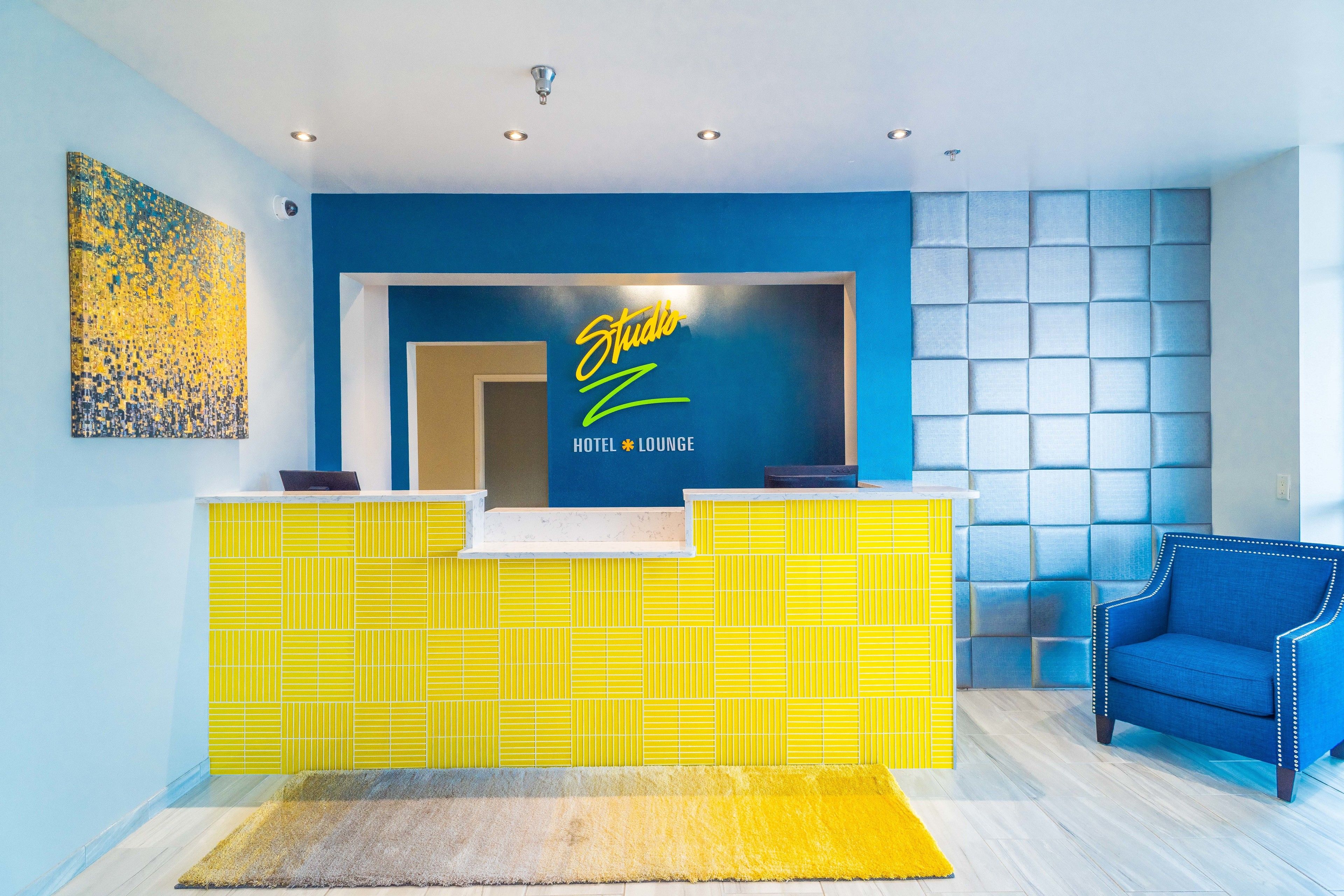 A hotel reception area with a blue wall, a yellow reception desk, and a blue armchair.