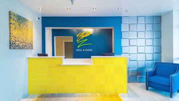 A hotel reception area with a blue wall, a yellow reception desk, and a blue armchair.
