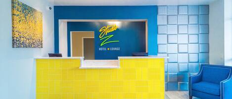 Ein Hotel-Empfangsbereich mit blauer Wand, einem gelben Empfangstresen und einem blauen Sessel.