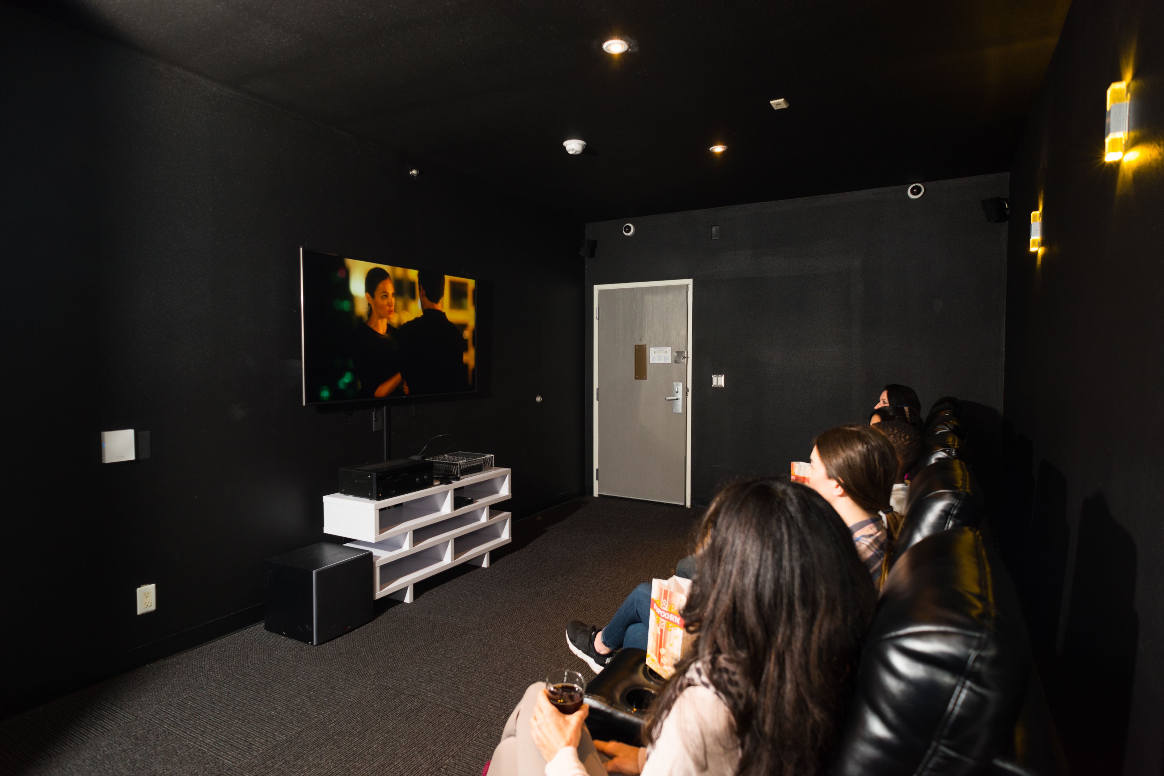 A dark room with a flat-screen TV mounted on the wall, a white entertainment unit, and a door.