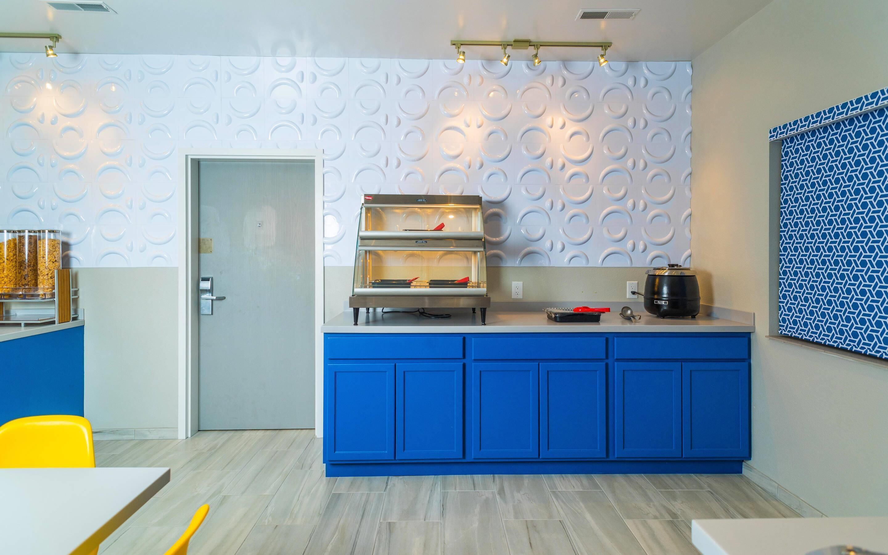 A modern kitchen with blue cabinets, a built-in oven, and a coffee machine.