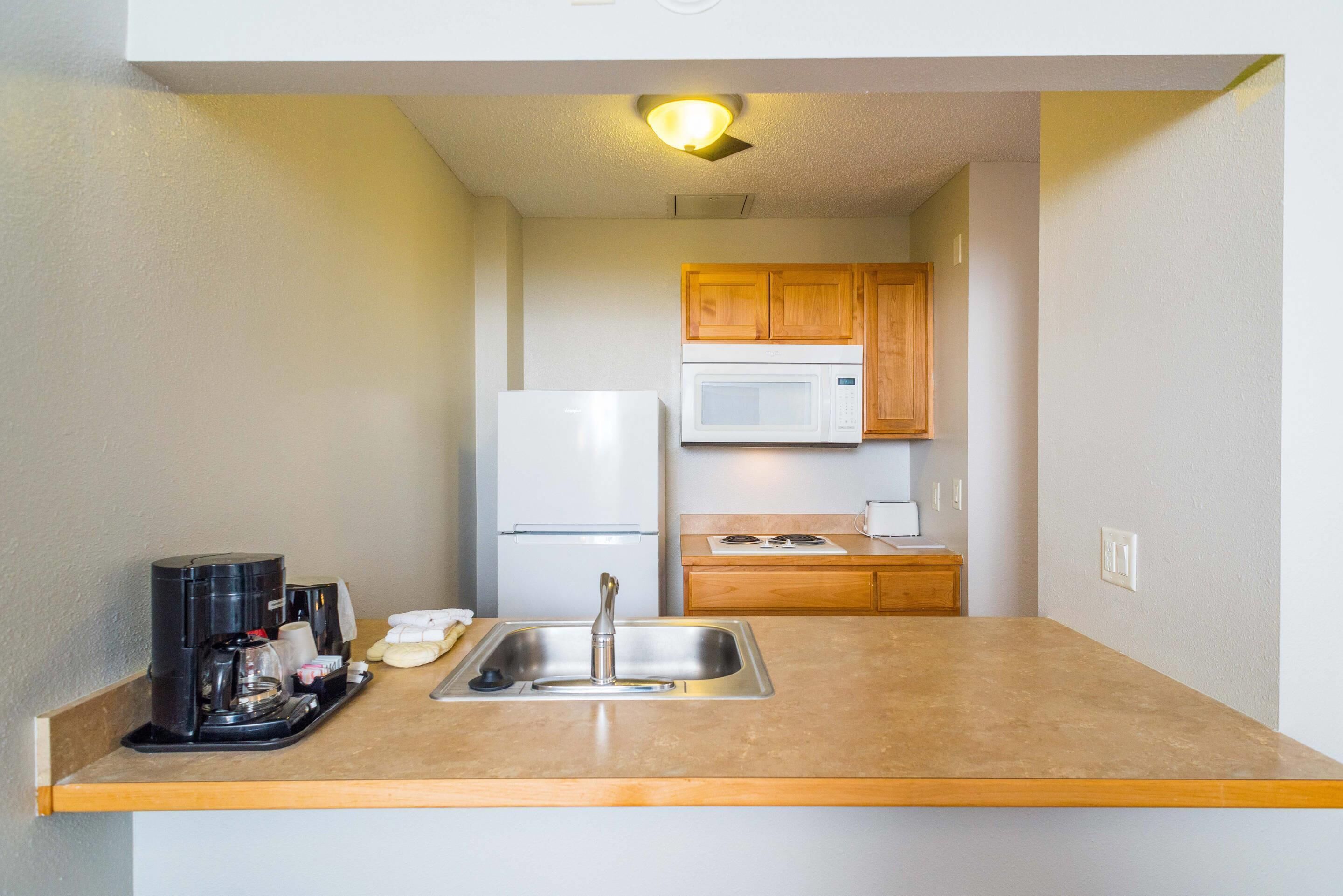 A compact kitchenette with a stainless steel sink, a microwave, a refrigerator, and wooden cabinets.