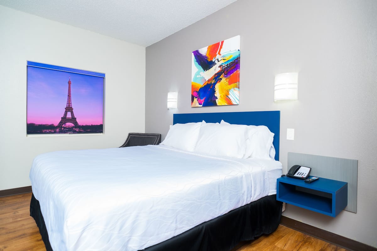 A hotel room with a large bed, a blue headboard, a bedside table with a phone, and two wall-mounted lights.