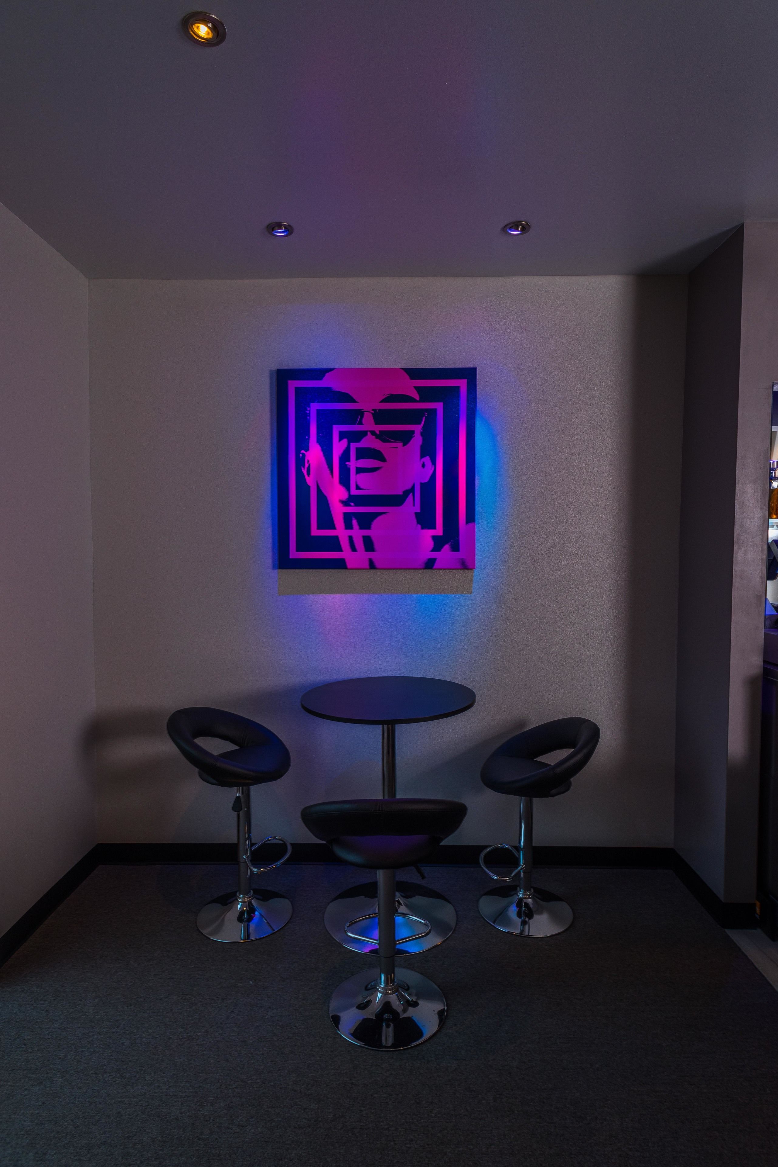 A room with a modern design, featuring a wall-mounted artwork, a small round table, and three bar stools.