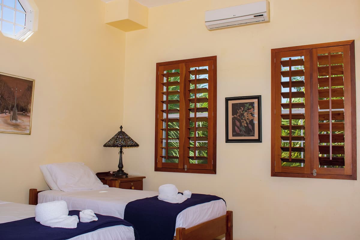 A hotel room with two beds, a nightstand, a lamp, and a painting on the wall.
