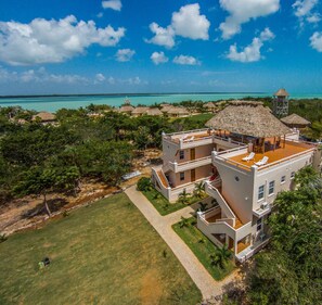 Um grande resort com vários edifícios, uma construção com telhado de palha e vista para o oceano.