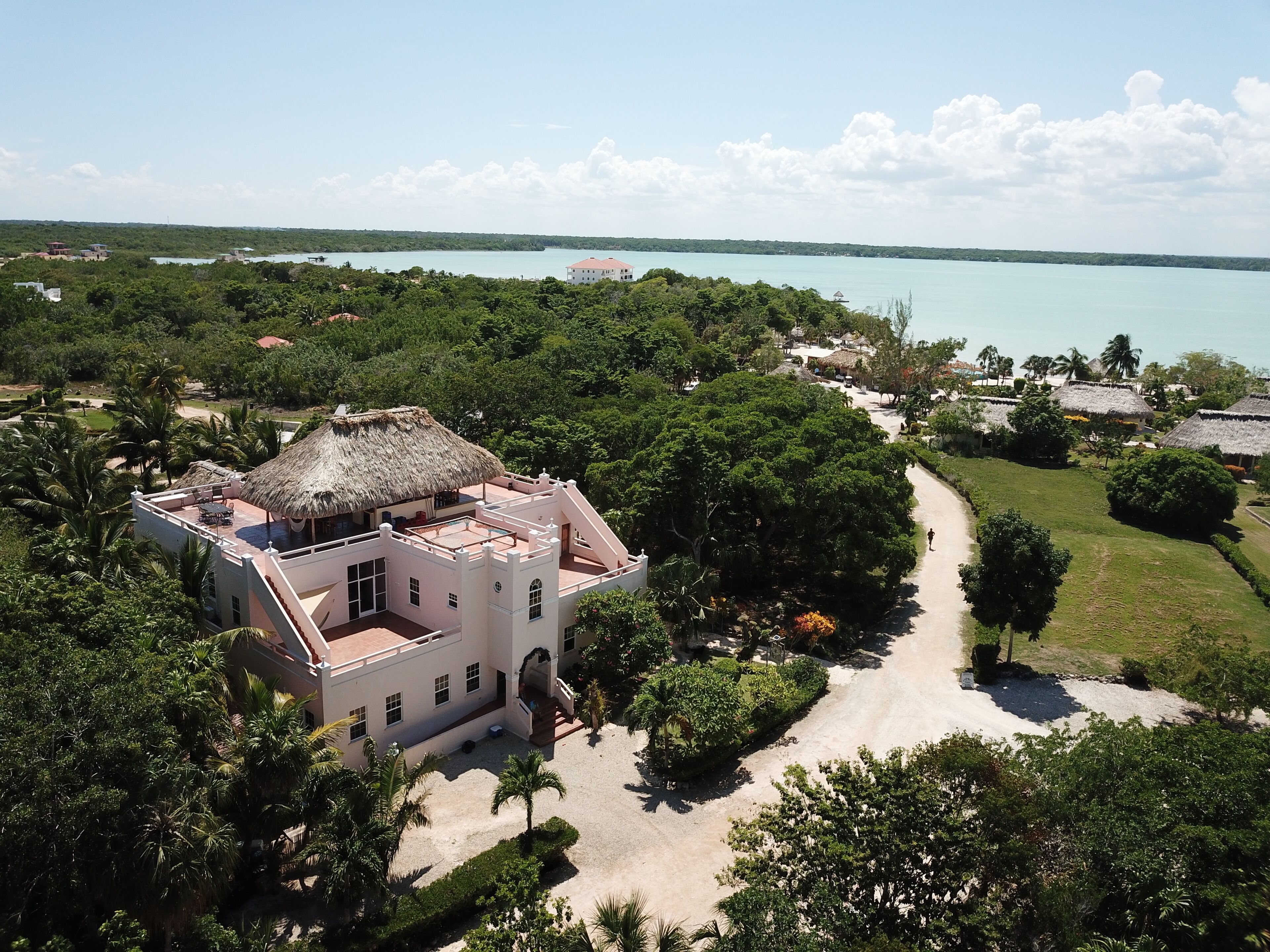 A large, multi-story building with a thatched roof, surrounded by lush greenery and a clear view of a large body of water.