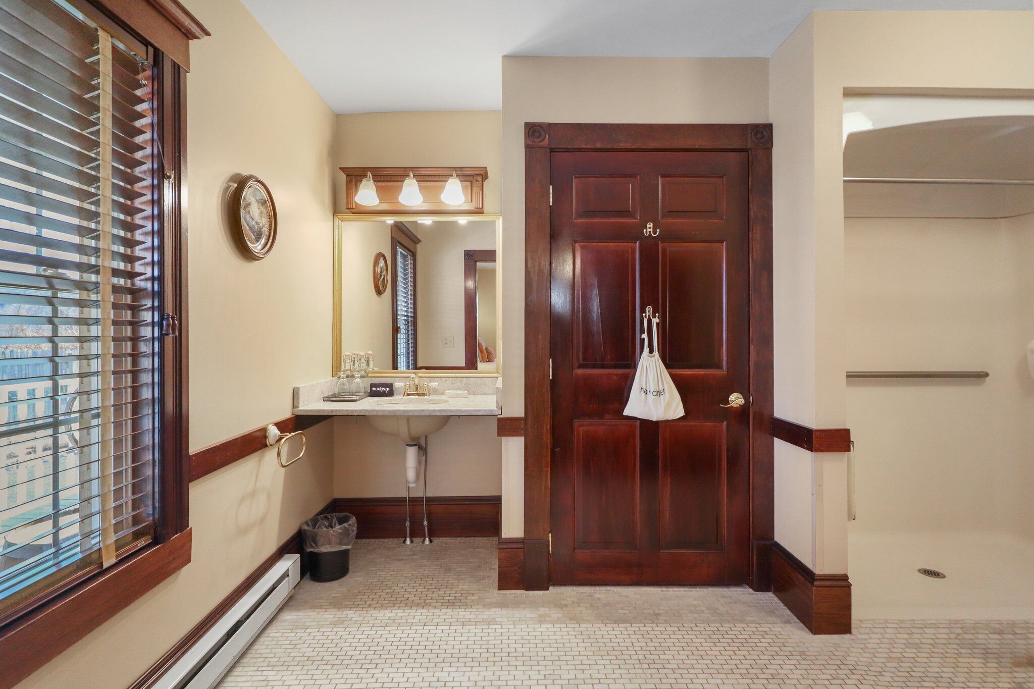A bathroom with a wooden door, a sink, a mirror, and a window with blinds.