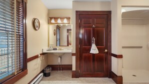 A bathroom with a wooden door, a sink, a mirror, and a window with blinds.