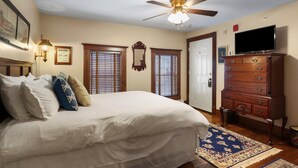 A bedroom with a bed, dresser, television, ceiling fan, and two windows with blinds. - Trainmasters Inn (Palmer)