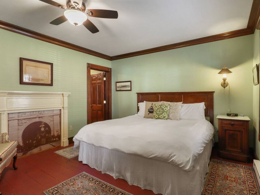 Une chambre à coucher avec un grand lit, une tête de lit en bois, une cheminée, un ventilateur de plafond et une table de chevet avec une lampe.