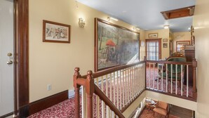 A staircase with a wooden railing leading to a second floor. There is a large framed painting on the wall, a door with a wooden frame, and a carpeted floor. - Trainmasters Inn (Palmer)