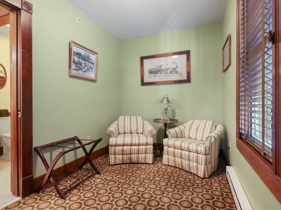 A room with two striped armchairs, a small table, and two framed pictures on the wall.