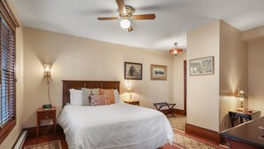 A neatly arranged bedroom with a large bed, bedside lamps, a ceiling fan, and a rug.