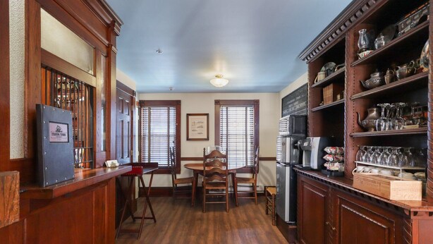 A wooden interior with a dining table and chairs, a refrigerator, and shelves with glassware. - Trainmasters Inn (Palmer)
