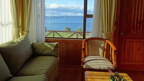 Une pièce avec vue sur un lac, une porte en bois, un canapé vert et une chaise en bois.