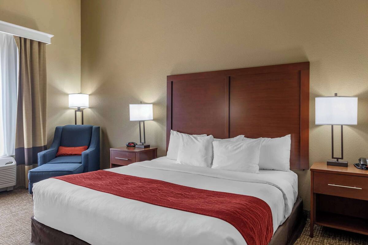 Quarto de hotel com uma cama grande, duas mesas de cabeceira, uma cadeira, um abajur e um criado-mudo.