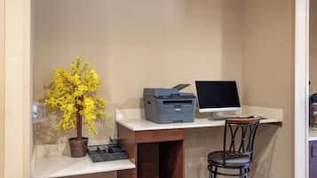 A small office space with a desk, a printer, a computer monitor, a chair, and a potted plant.