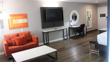 Een hotelkamer met een grote flatscreen-tv, een bureau met stoel, een bank en een bed.