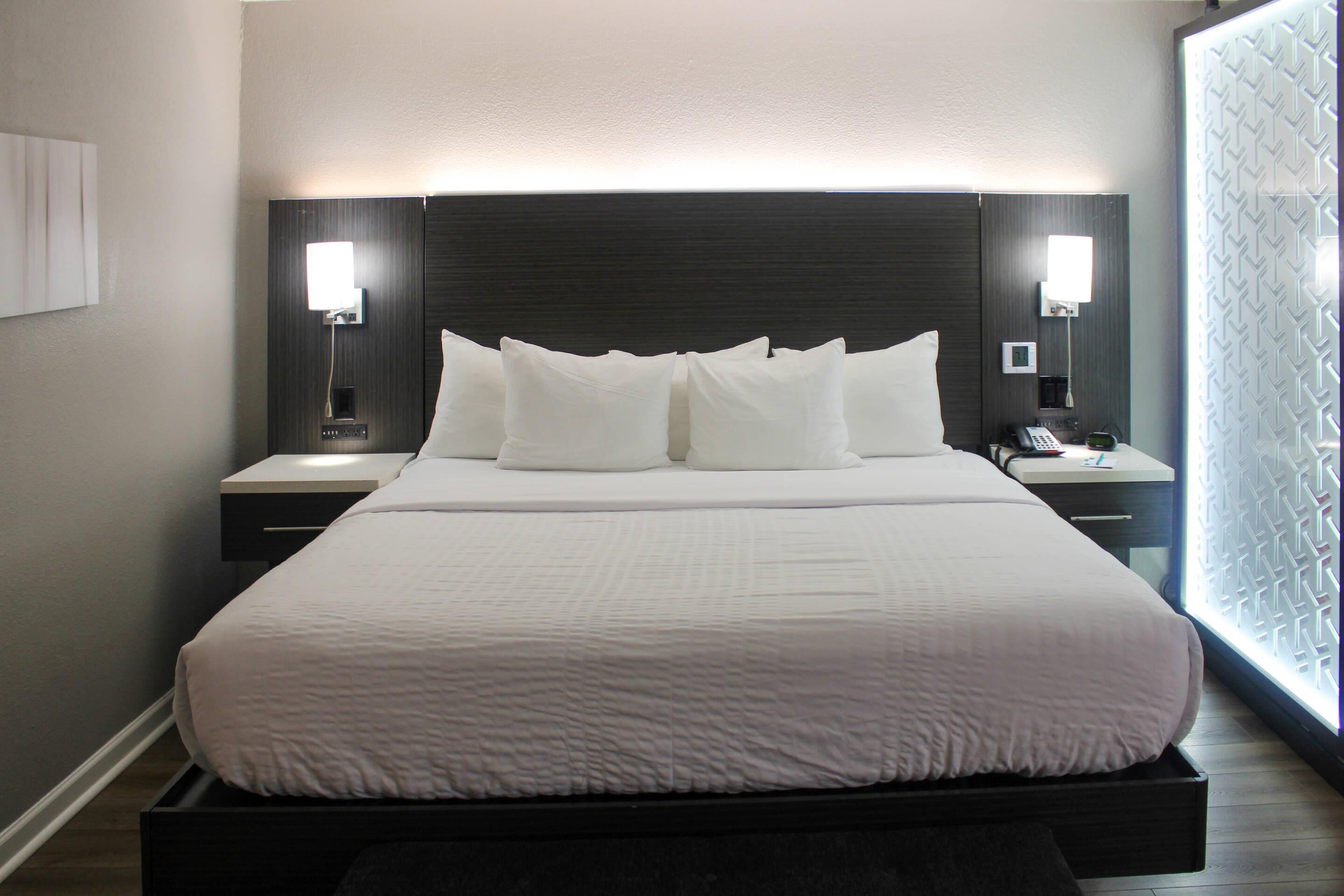 A modern hotel room with a large bed, two bedside tables, and a nightstand with a lamp.