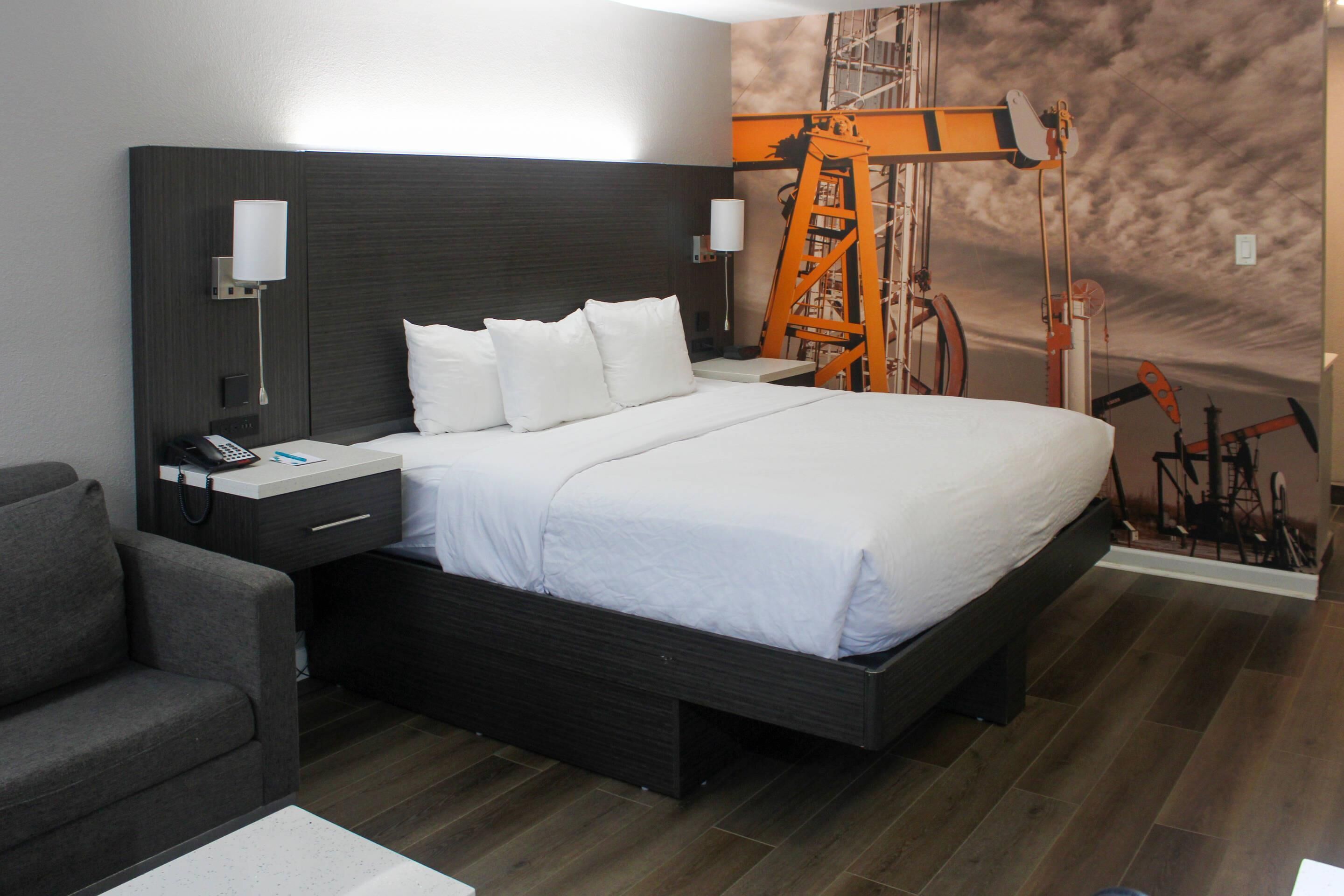 A modern hotel room with a large bed, a nightstand with a phone, a lamp, and a wall-mounted light.