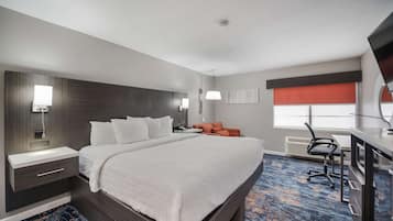 Una habitación de hotel con una cama grande, un escritorio con silla, una mesita de noche y un televisor montado en la pared.