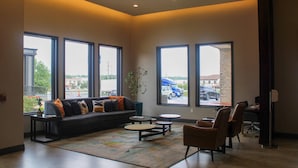 A spacious lobby with a large sofa, round tables, and comfortable seating. Large windows offer views of the outside. - Clarion Pointe Marshall (Marshall)