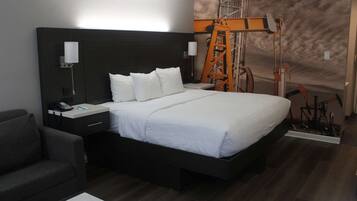 Una habitación de hotel moderna con una cama grande, una mesita de noche con lámpara, un escritorio pequeño y una silla.