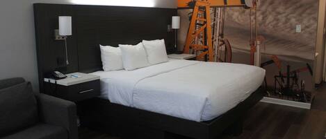 Una habitación de hotel moderna con una cama grande, una mesita de noche con lámpara, un escritorio pequeño y una silla.
