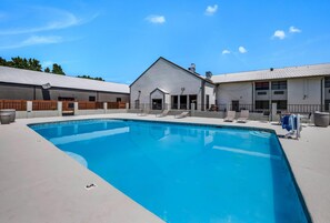 A swimming pool with a clear blue water, surrounded by a white building with a grey roof, and a fenced area with lounge chairs. - Clarion Pointe Marshall (Marshall)