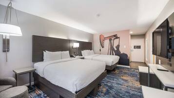Ein Hotelzimmer mit zwei Betten, einem Schreibtisch, einem Sessel, einer Lampe und einem Fernseher.