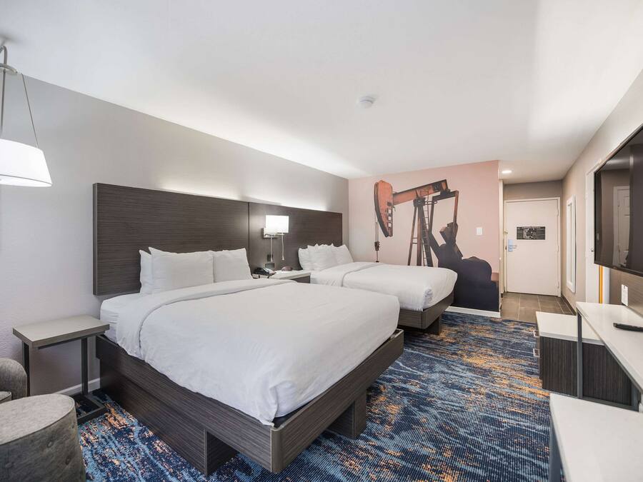 Ein Hotelzimmer mit zwei Betten, einem Schreibtisch, einem Sessel, einer Lampe und einem Fernseher.