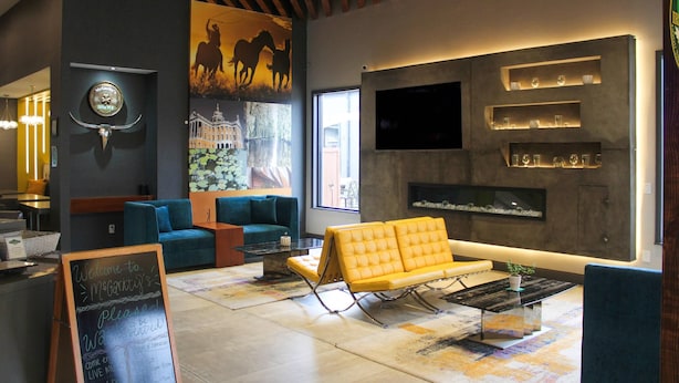 A modern lobby with a yellow sofa, blue armchairs, a fireplace, and a large mural. - Clarion Pointe Marshall (Marshall)
