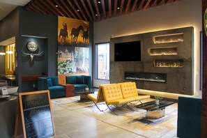 A modern lobby with a yellow sofa, blue armchairs, a fireplace, and a large mural. - Clarion Pointe Marshall (Marshall)
