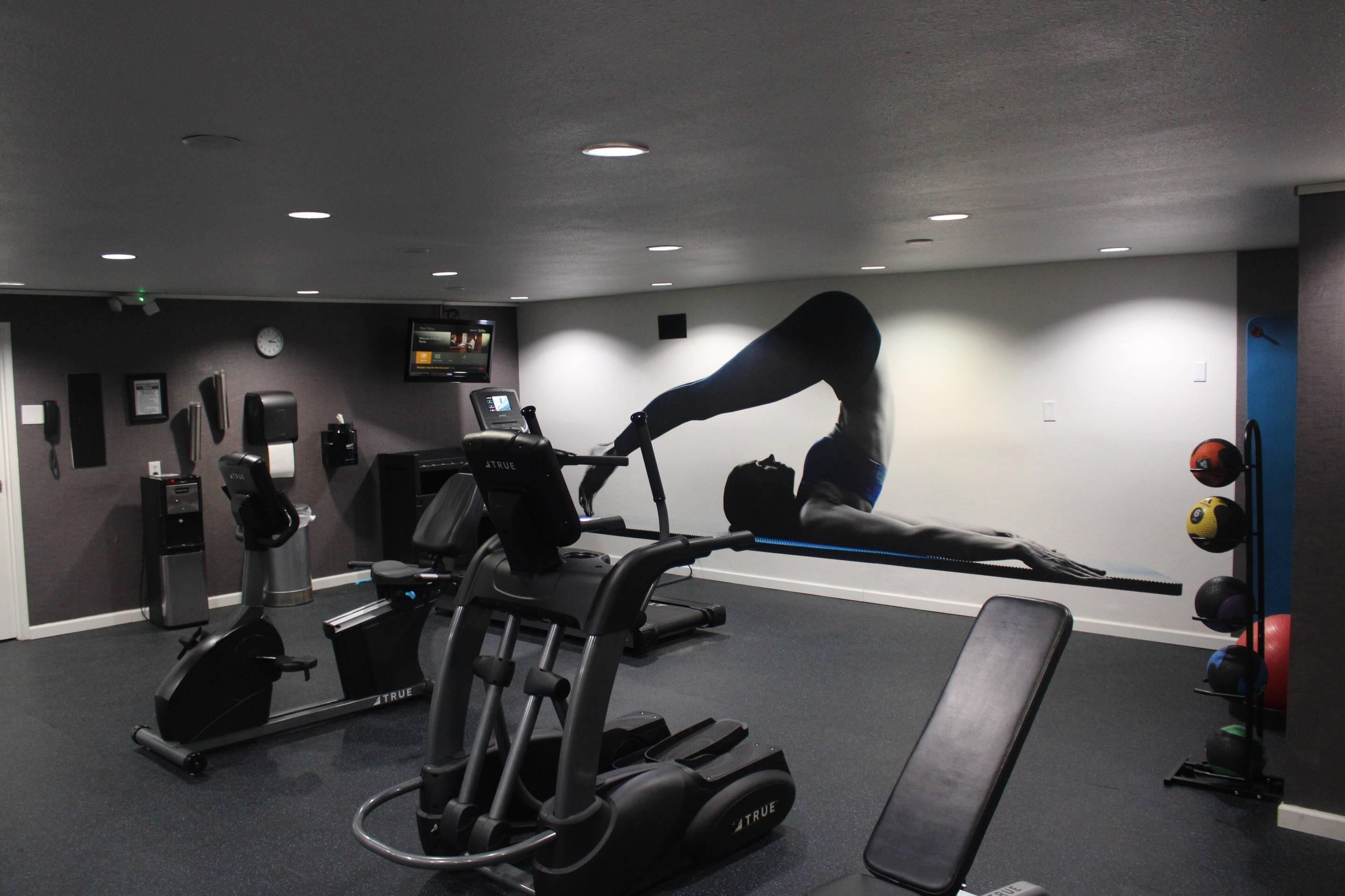 Une salle de sport équipée de matériel d’exercice, avec un téléviseur et une horloge au mur.