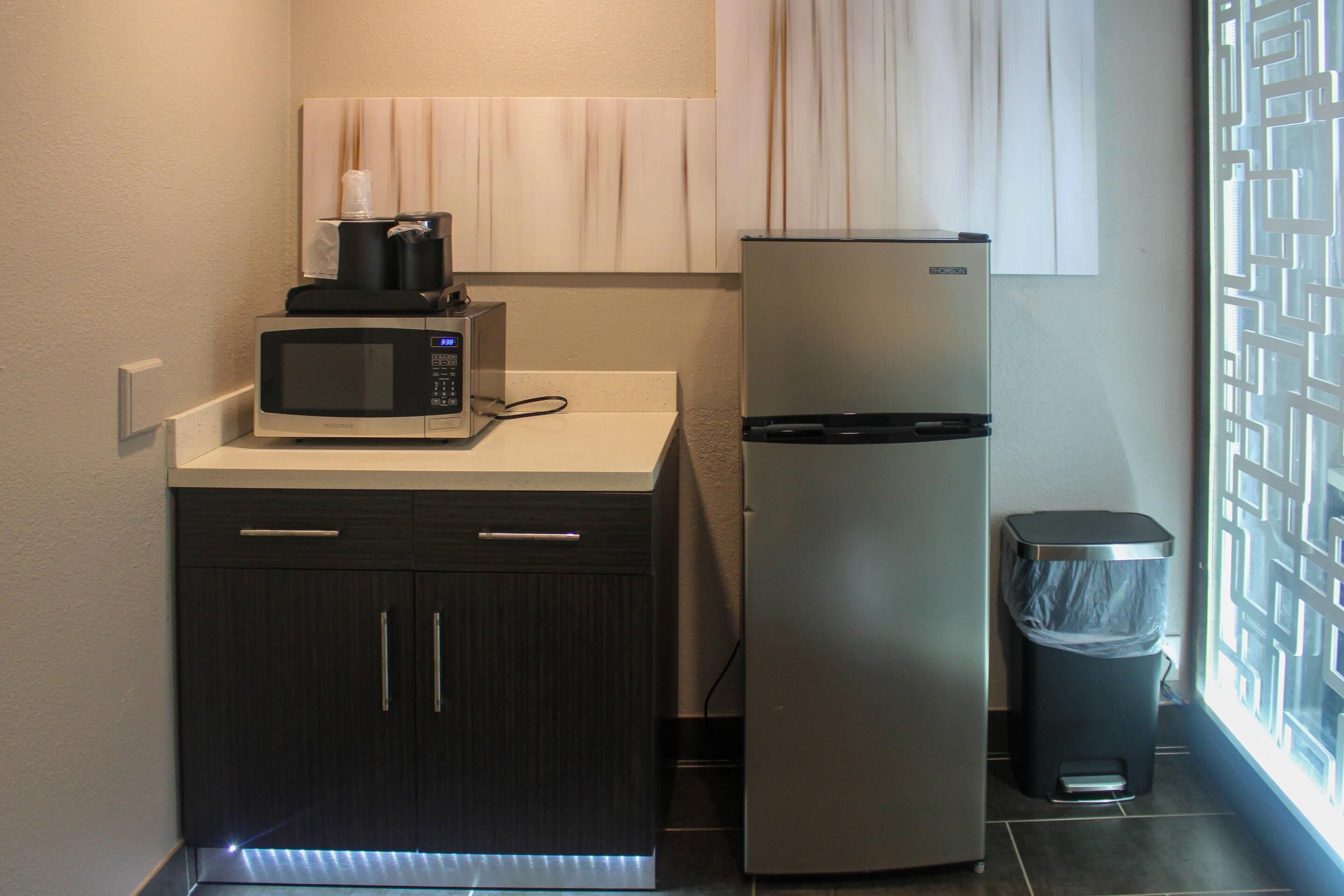 A compact kitchenette with a microwave, coffee maker, refrigerator, and trash bin.