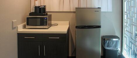 A compact kitchenette with a microwave, coffee maker, refrigerator, and trash bin.