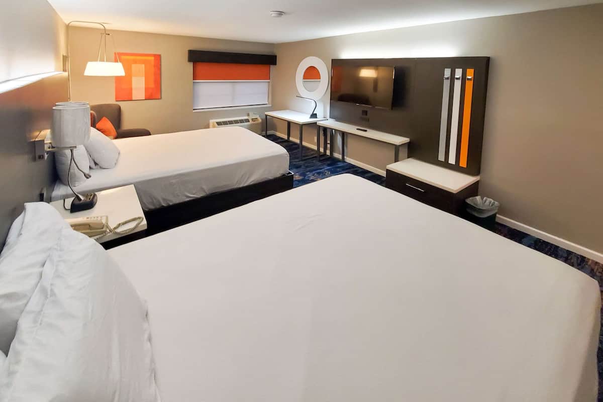 A hotel room with two beds, a desk, a chair, a TV, and a large mirror.