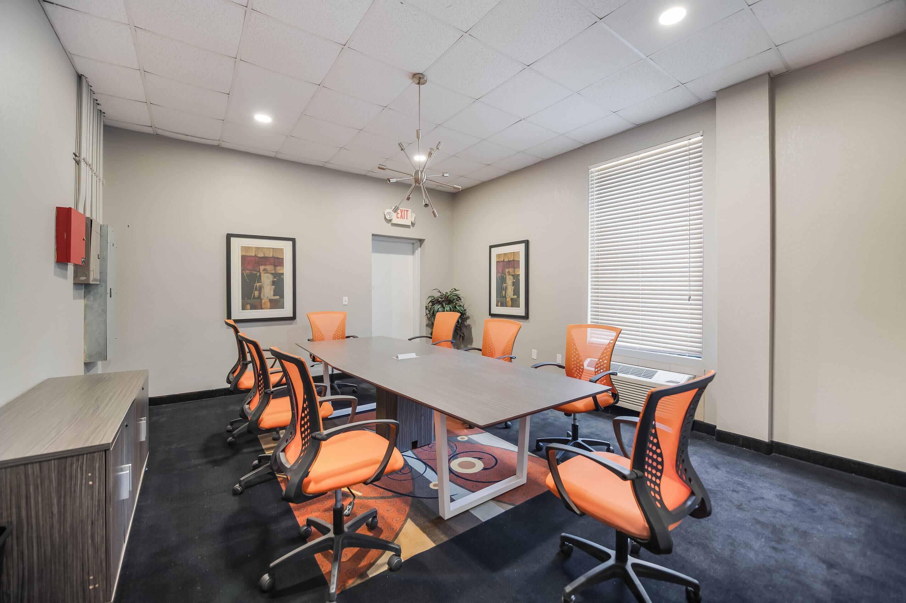 A conference room with a long table, orange chairs, a whiteboard, and a ceiling light.