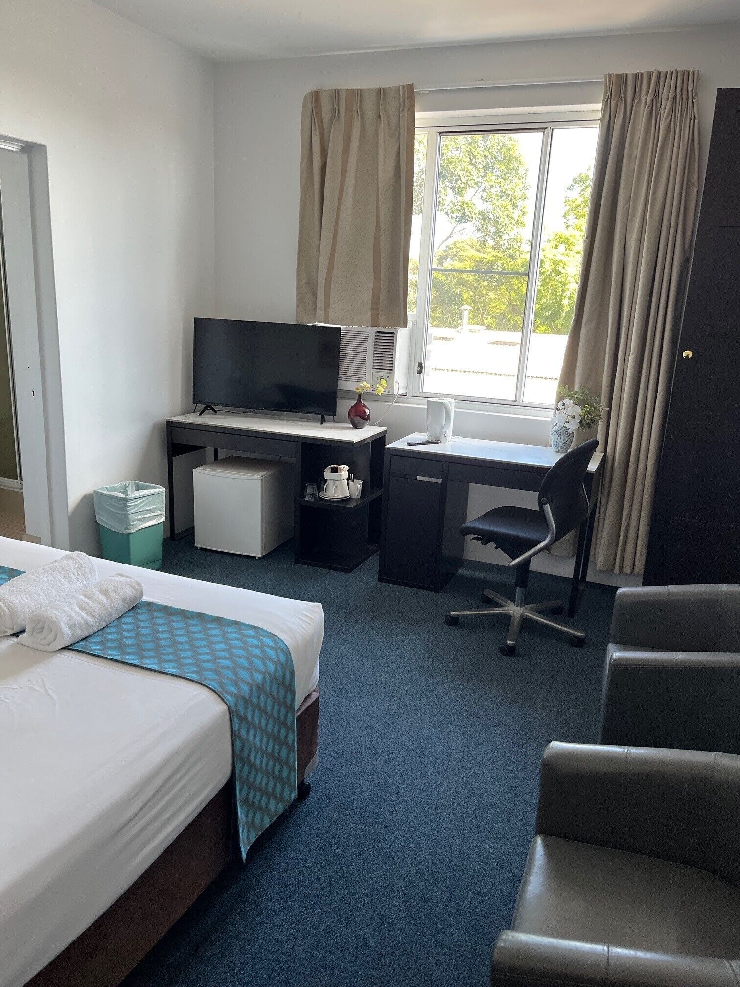A hotel room with two beds, a desk with a television, a chair, and a window with curtains.