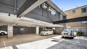 En parkeringskælder med to parkerede biler, betongulve og en bygning med ventilationsanlæg.