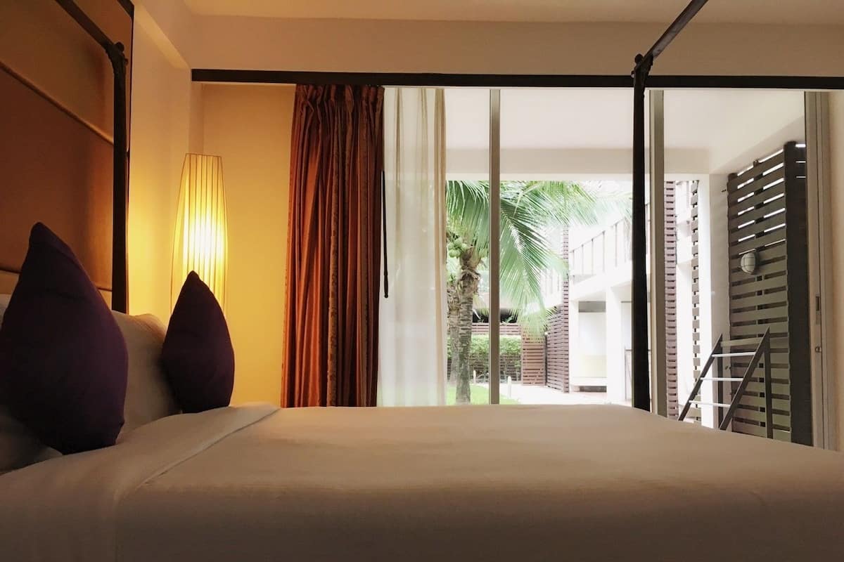 Een hotelkamer met een bed, een lamp, uitzicht op een binnentuin met palmbomen en een trap.