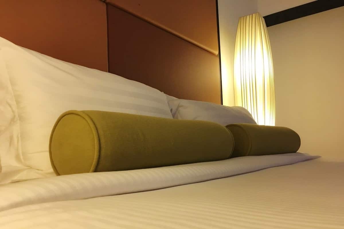Een opgemaakt bed met witte lakens en twee groene kussens.